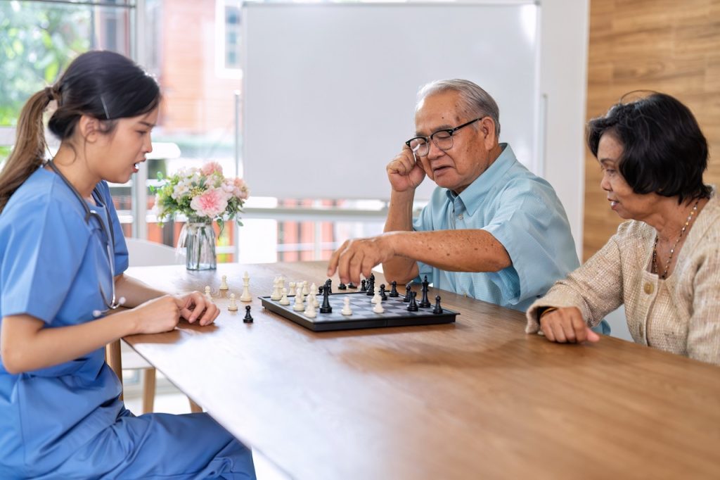 Caregiver take care elderly retirement sitting and play chess together think on strategy to win