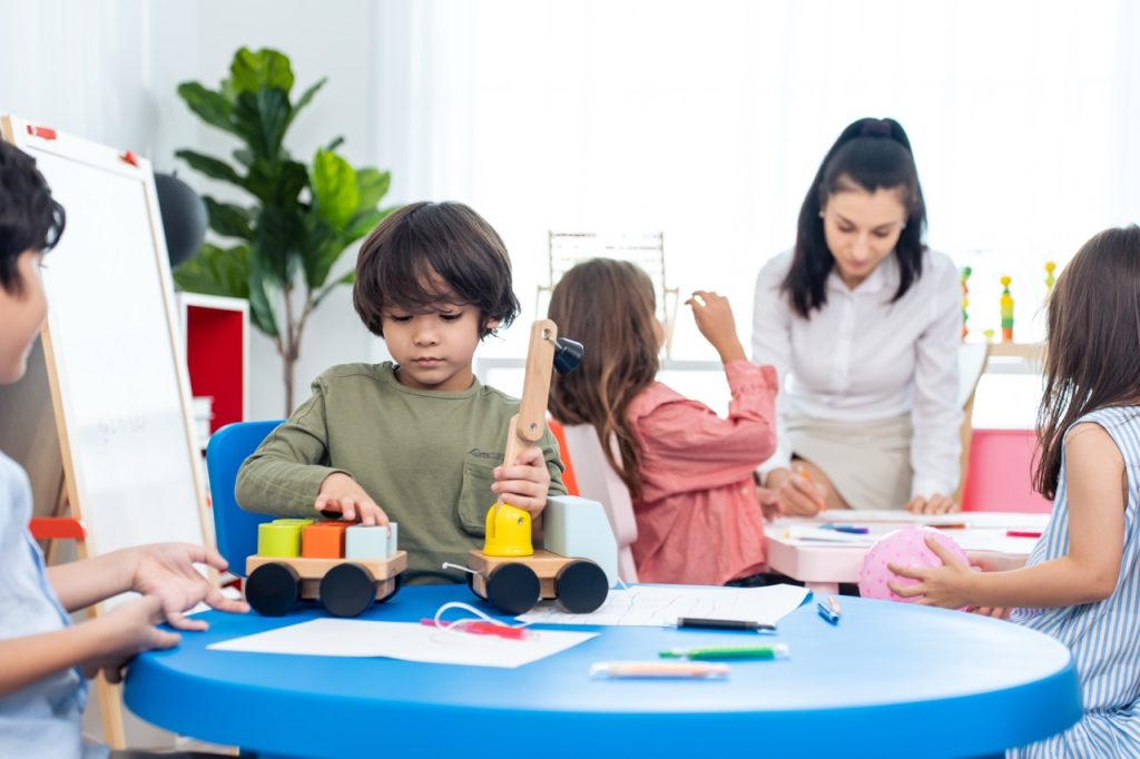 Caucasian beautiful young woman teacher teaching art to kids at school. Attractive Instructor master female explain and educate drawing and painting with student kindergarten pre school in classroom.
