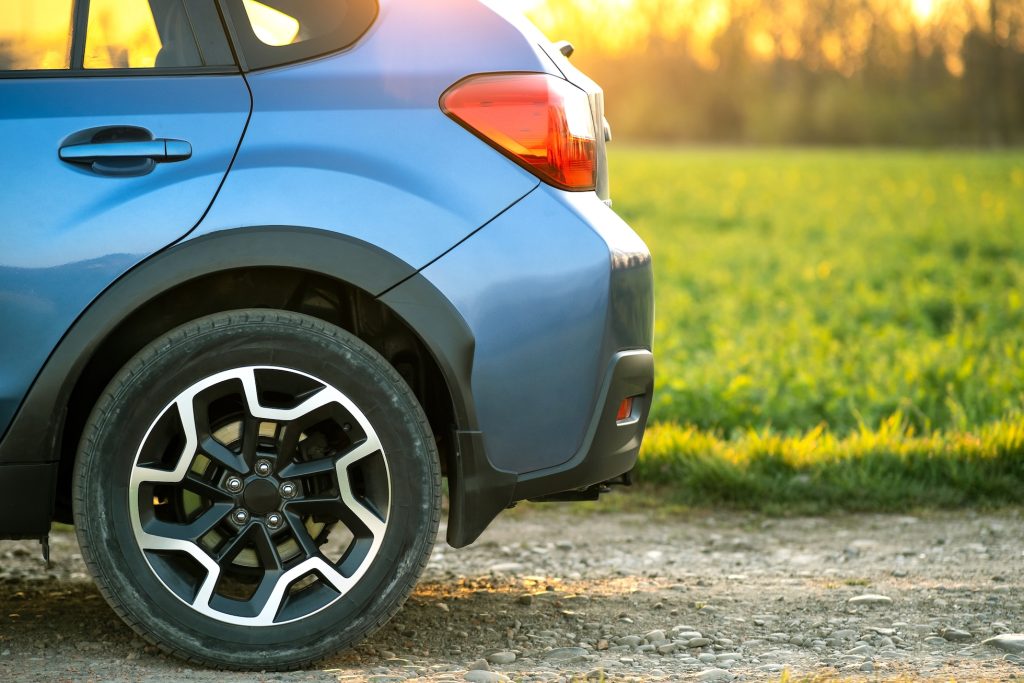 Close up of blue off road car wheel on gravel road. Traveling by auto, adventure in wildlife, expedition or extreme travel on a SUV automobile. Offroad 4x4 vehicle in field at sunrise.