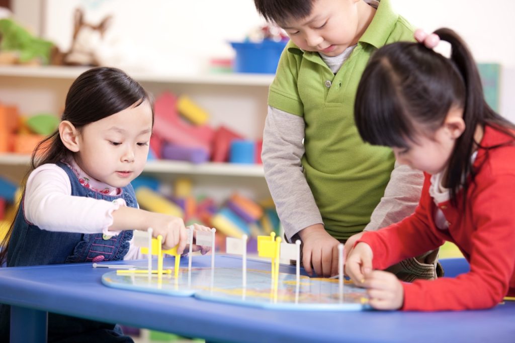Cute Chinese kindergarten children placing flags on world map
