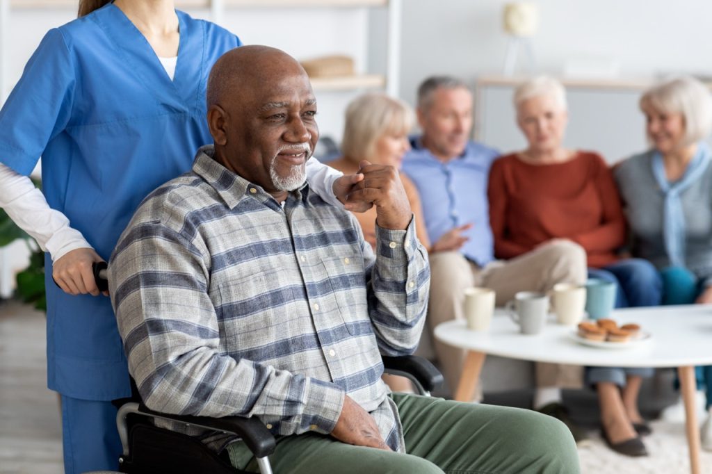 Disabled african american senior man in wheelchair holding nurse hand, looking at copy space and smiling, thanking for support, life in nursing home for elderly people concept