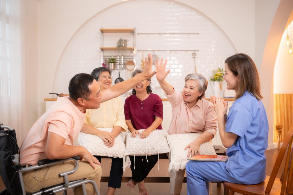 Group of elderly and senior man in wheelchair with nurse at nursing home Play a fun game of hitting each other's hands. Elderly people in nursing home concept