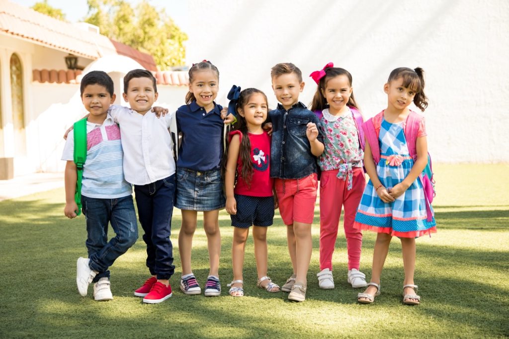Full length view of a group of kids standing outside of preschool on a sunny day and smiling