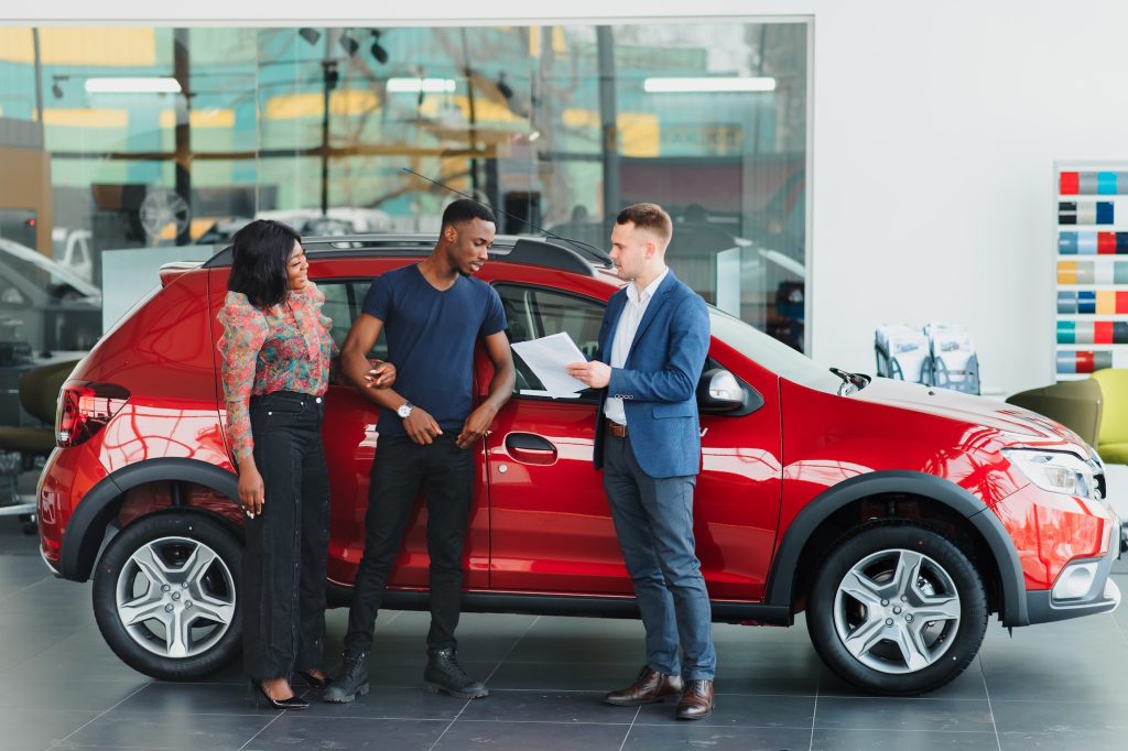 happy african couple choosing luxury car at vehicle dealership looking at the interior