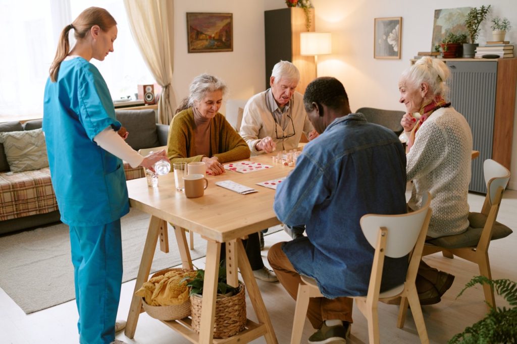 Wide shot of nurse pouring water while group of biracial senior people playing bingo at table