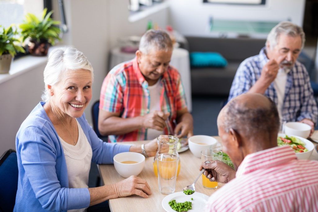 Portrait of senior woman sitting with friends while having breakfast at table in nursing home
