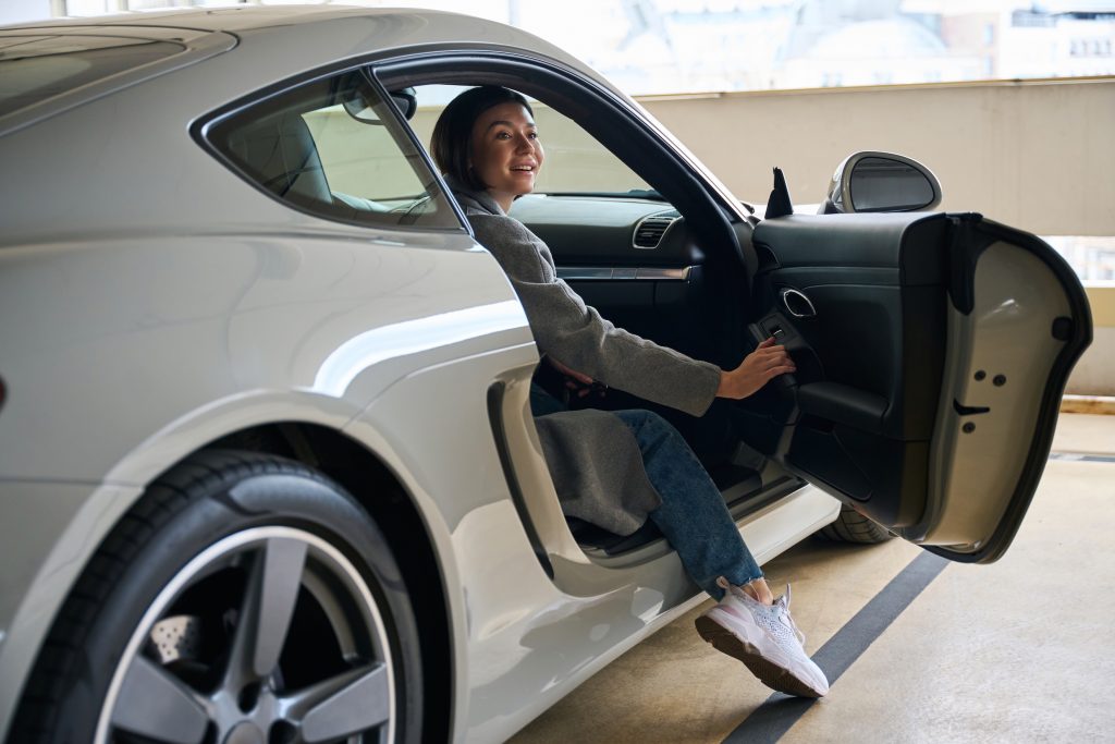 Beautiful attractive female passenger getting into or out of car in mall parking lot