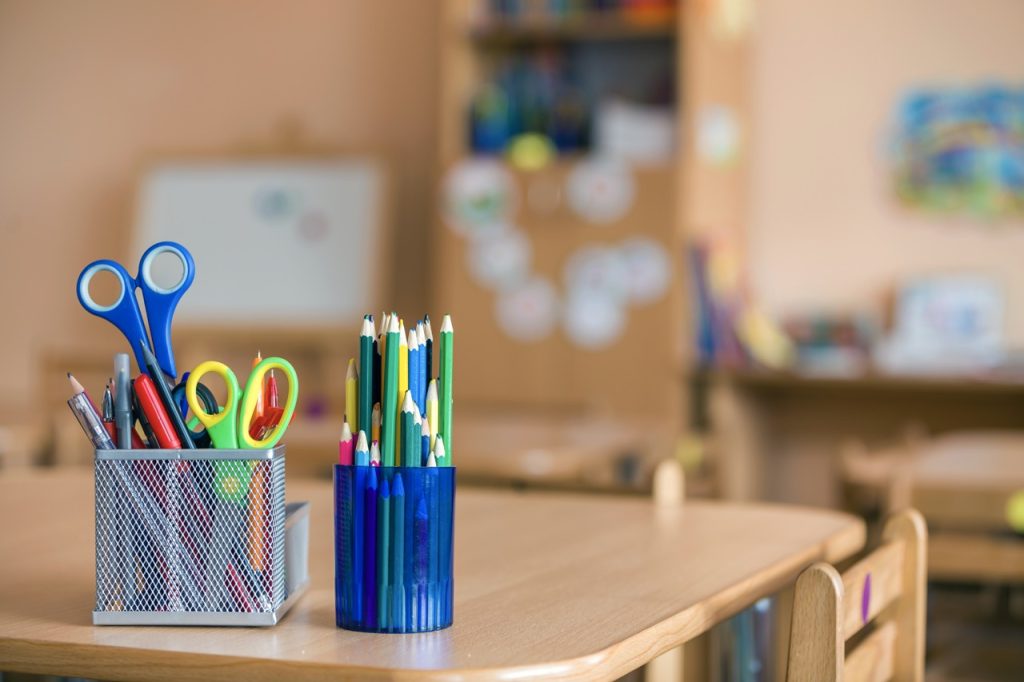 Stack of notebooks, colorful drawing pencils and stationery arrangement on copy space background.