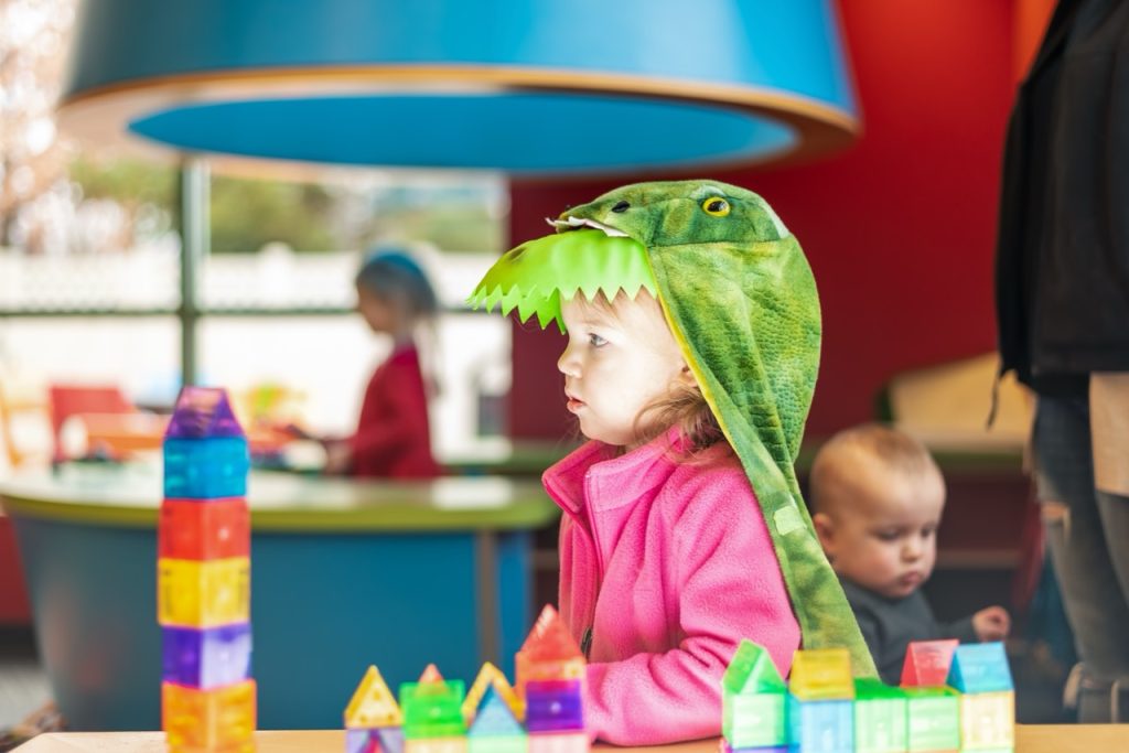 Toddler girl dressed in a dinosaur costume playing with toys - creative play